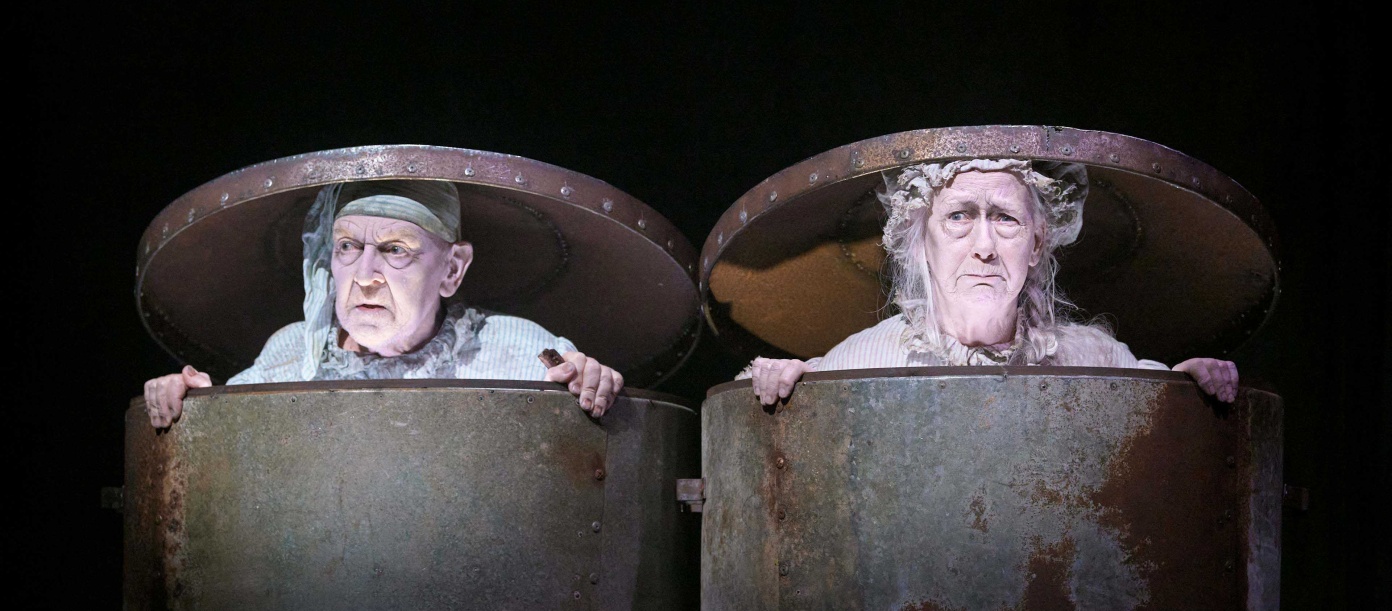 A black-and-white photograph of two people in trash cans with the lids on top of their heads.