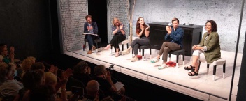 A group of five people seated on stools on the stage of The Mick Lally Theatre with some audience members visible in the left corner.