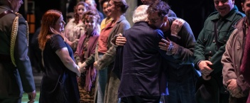 President Higgins with his back to the camera speaks to a group of actors on stage.