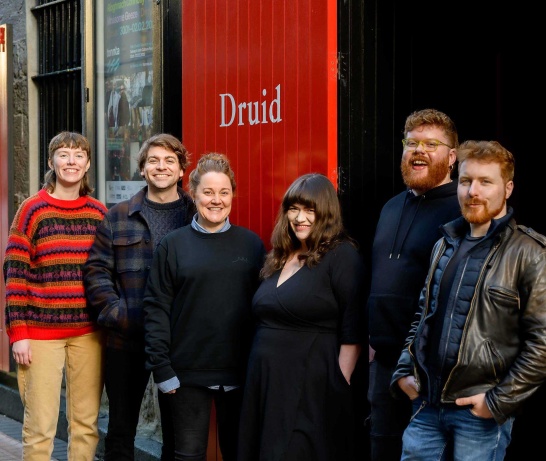 Six people pose together outside The Mick Lally Theatre on Druid Lane.