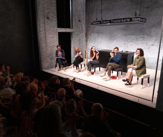 A group of five people seated on stools on the stage of The Mick Lally Theatre with some audience members visible in the left corner.