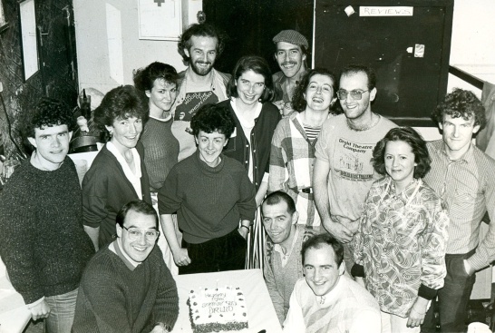 A black-and-white group photo featuring a large 10th anniversary cake.