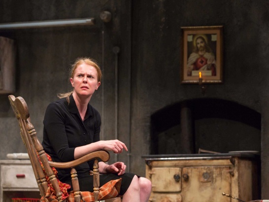A production photo of Martin McDonagh's The Beauty Queen of Leenane featuring Aisling O'Sullivan as Maureen Folan seated in the kitchen.