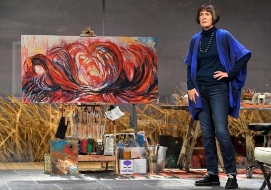A production photo of The Beacon by Nancy Harris featuring Jane Brennan stood in front of a large painting on an easel.