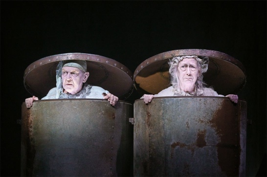 A production photo from Endgame featuring Bosco Hogan and Marie Mullen dressed in pyjamas and sat in adjoining dustbins.