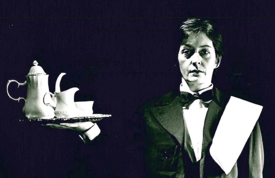 A black-and-white production photo from The Singular Life of Albert Nobbs featuring actor Jane Brennan in the lead role of the hotel butler, holding a tray and starting directly at the camera.
