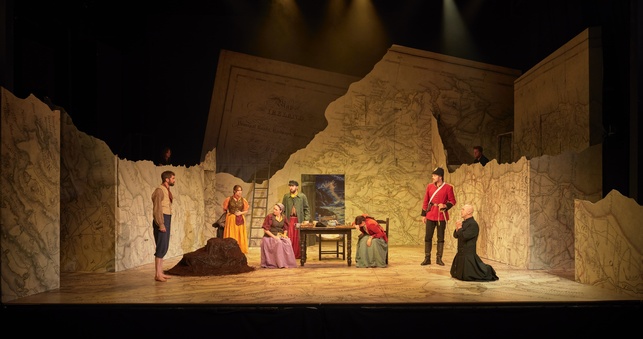 Part of the ensemble cast of The Shaughraun sit and stand around a table.
