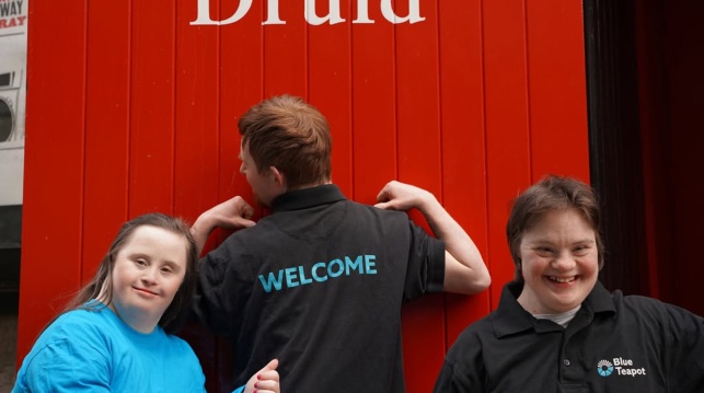 Three people pose for a photo in front of the red Druid door on Druid Lane.