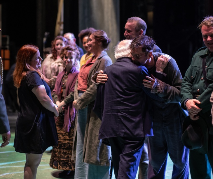 President Higgins with his back to the camera speaks to a group of actors on stage.