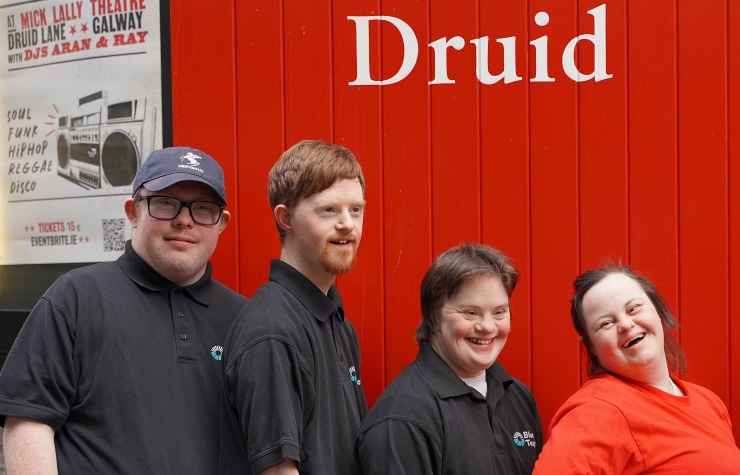 Four people stand outside the theatre with the red Druid door behind them.
