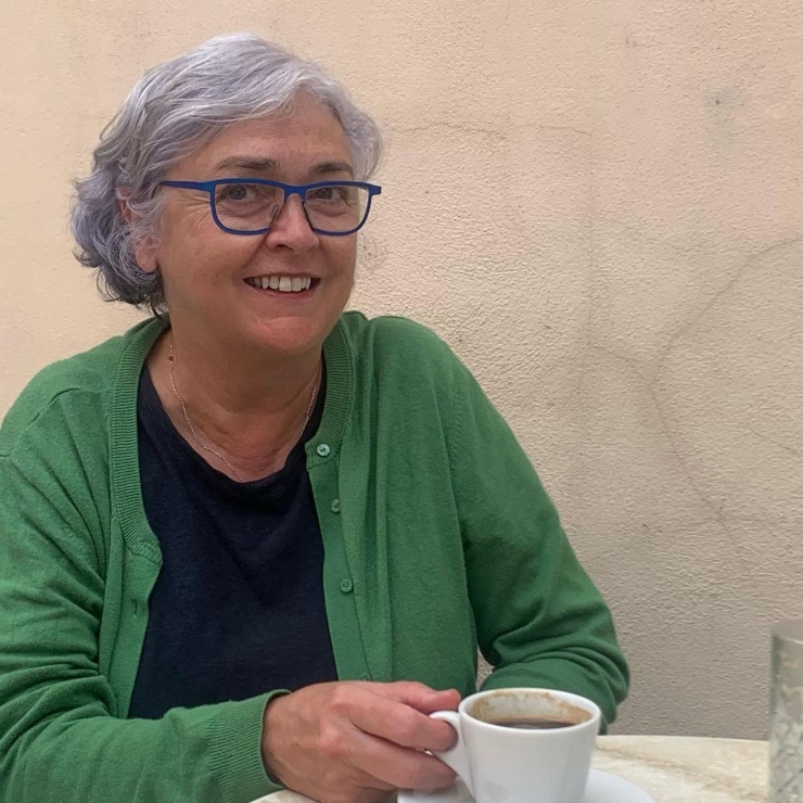 Martha O'Neill, wearing a green cardigan and sat at a table with a cup in her hand, smiles to the camera.
